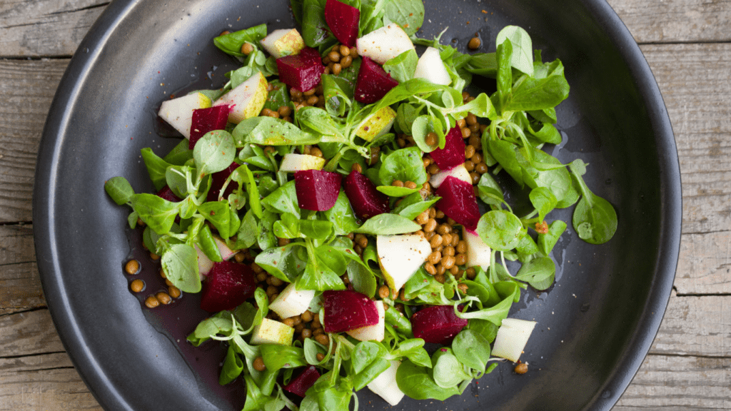 a salad with beets, apples and greens on a black plate